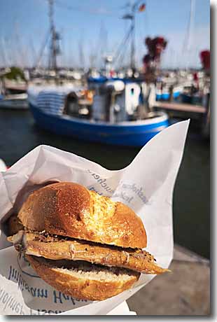 Fischbrötchen-Genuss im Hafen Maasholm Frisches Fischbrötchen mit geräucherter Makrele im Hafen von Maasholm vor einem Fischerboot an der Schlei.