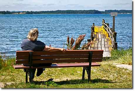 Auszeit an der Geltinger Bucht Frau sitzt auf einer Parkbank an der Geltinger Bucht in Wackerballig mit Blick auf den hölzernen Steg und das Wasser